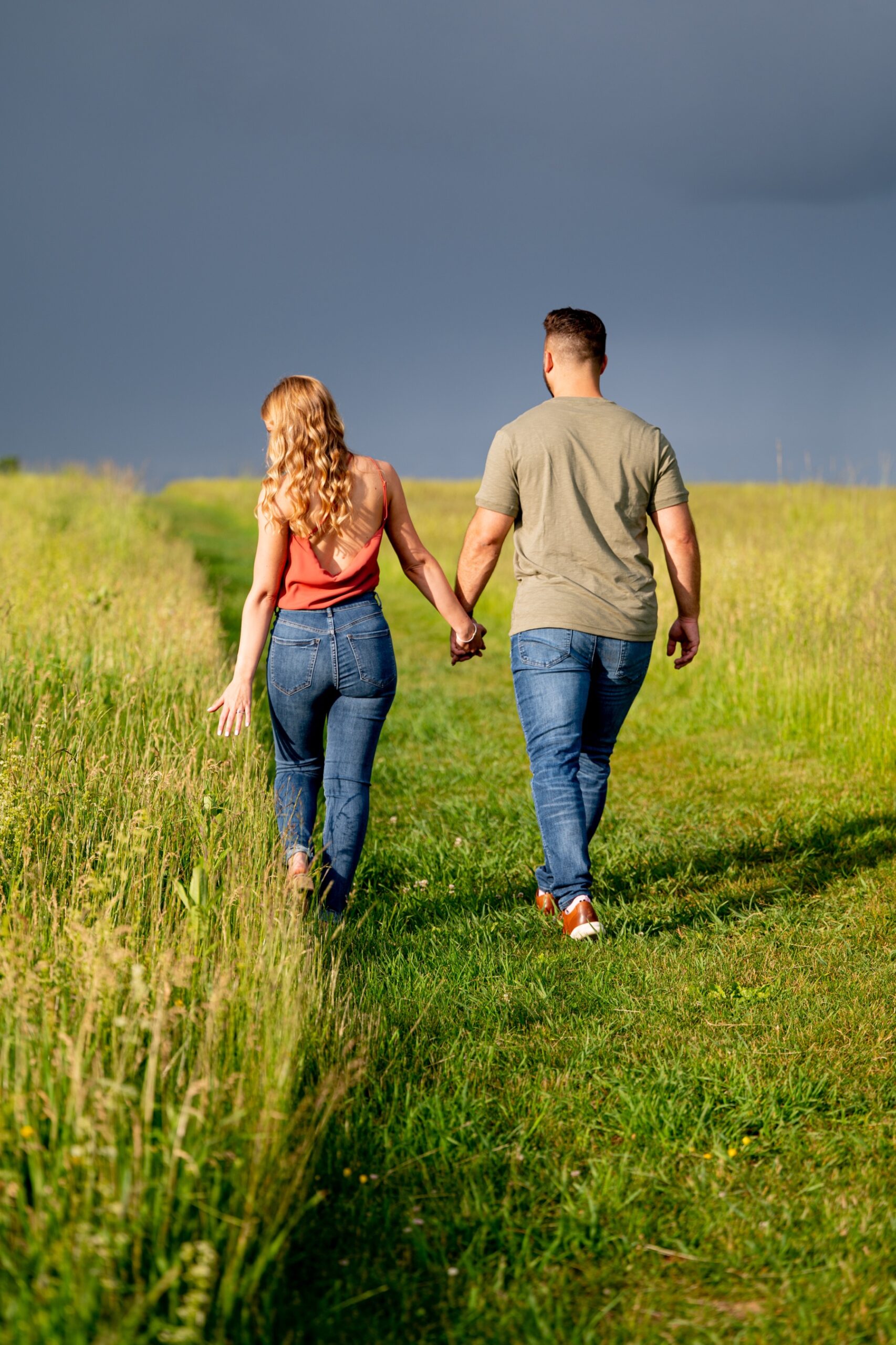 couple holding hands as they walk through a field of tall green grass