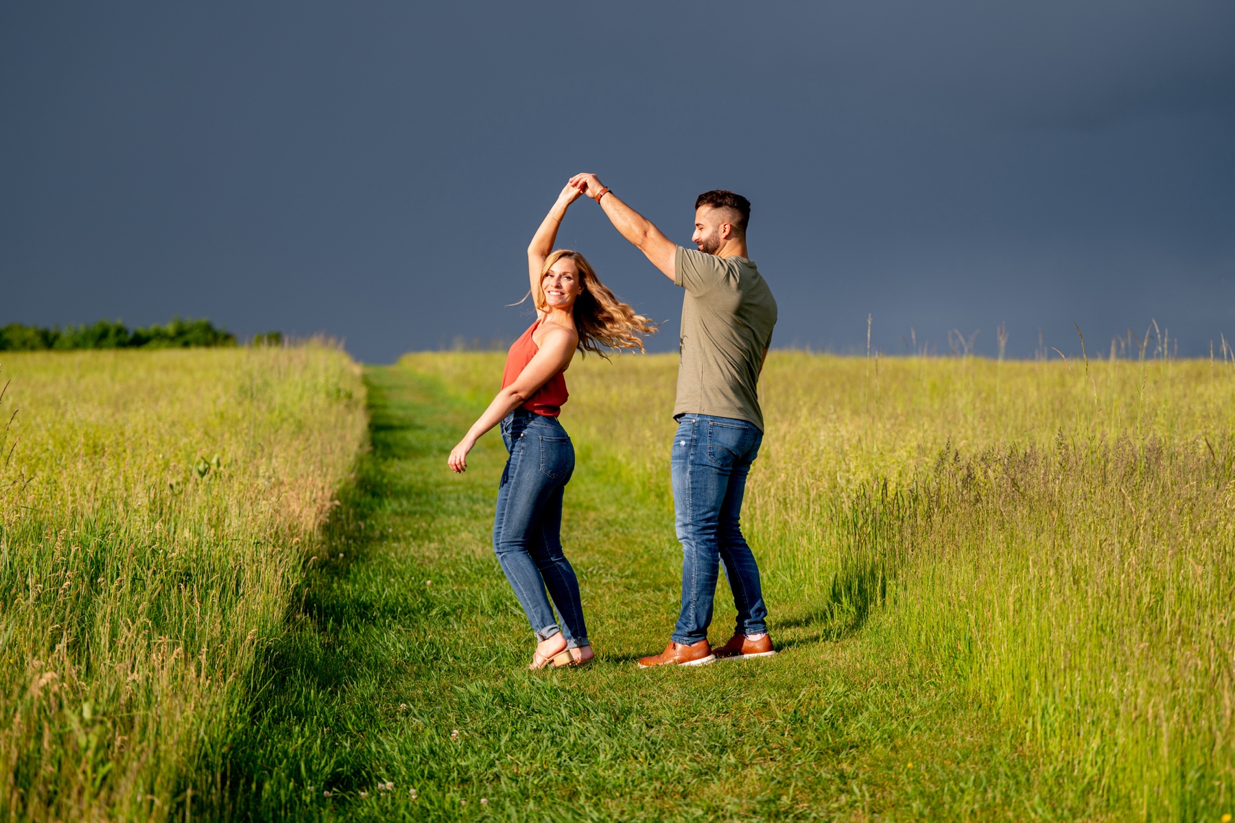 man twirling his fiance in a field of tall green grass