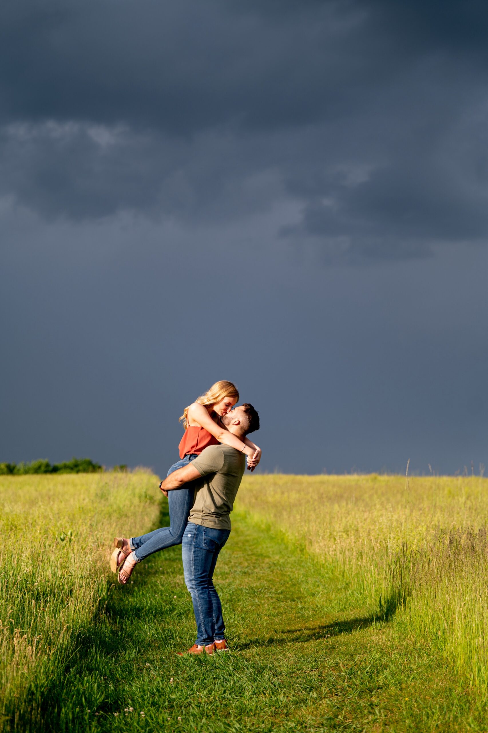 couple kissing in a field of tall green grass with dark storm clouds behind them