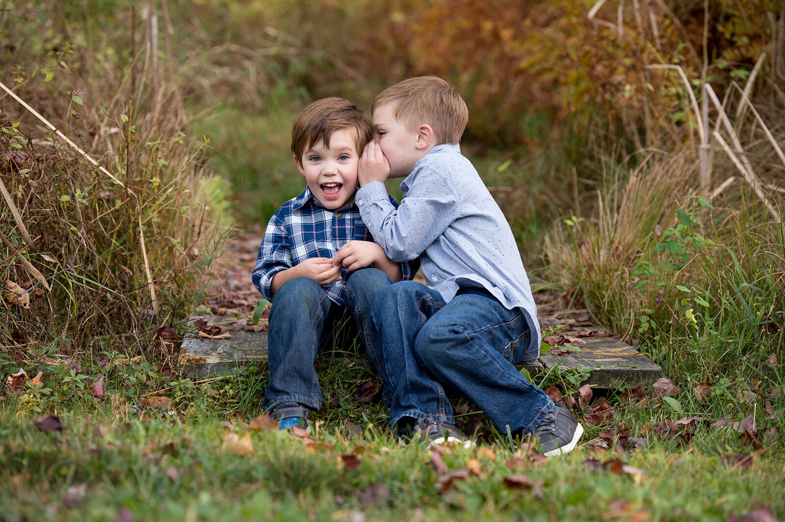 little boy whispering in another boy's ear while sitting on the ground for family portraits