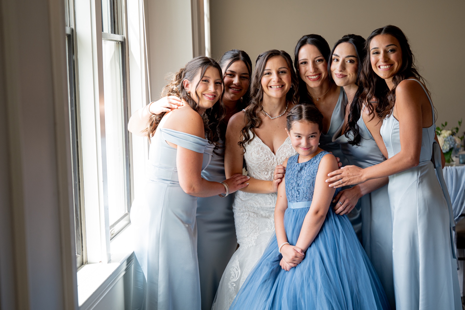 bride and her bridesmaids wearing light blue standing in a group and smiling at camera