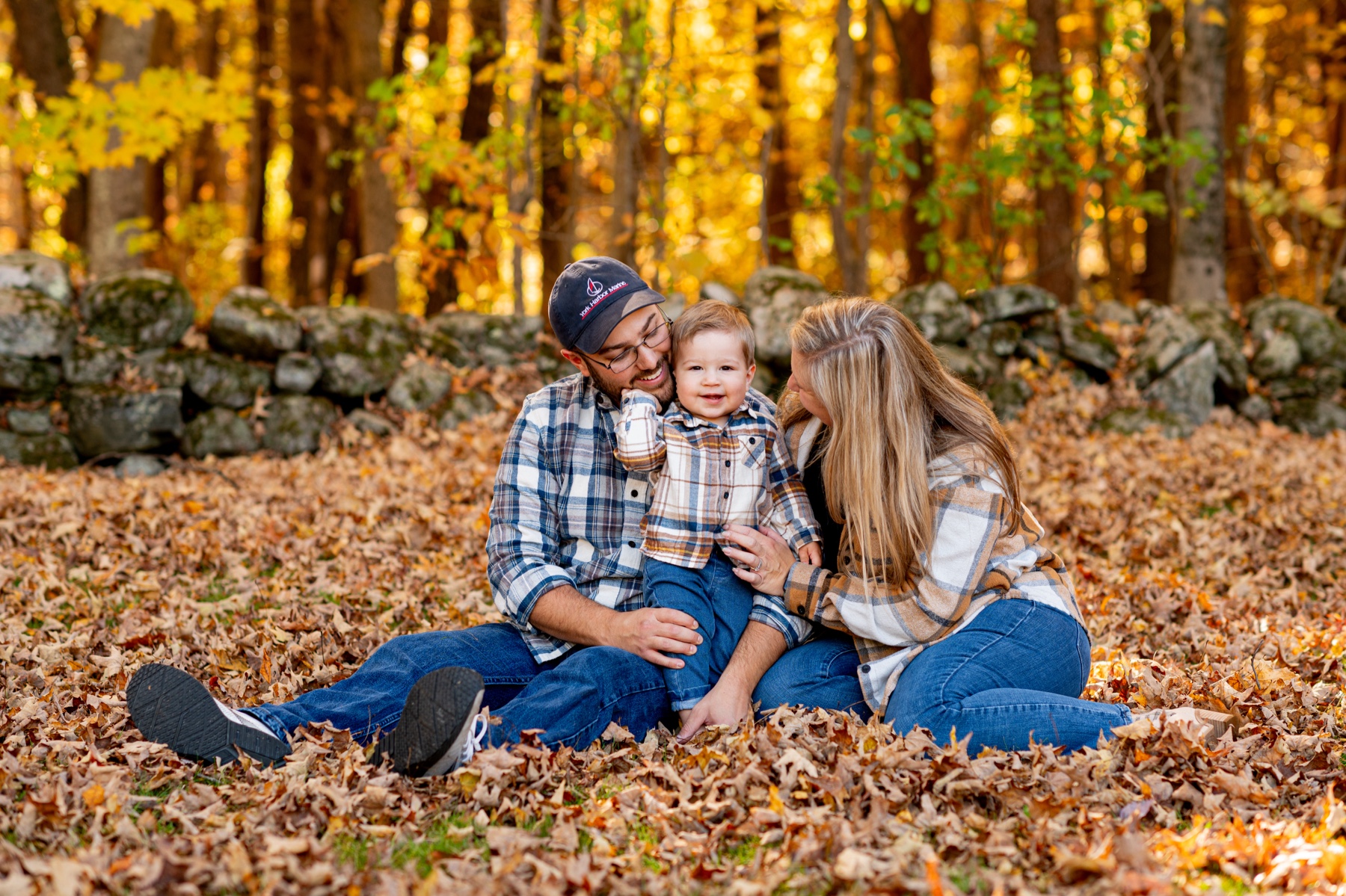 mother and father sitting with their young son on a pile of orange leaves