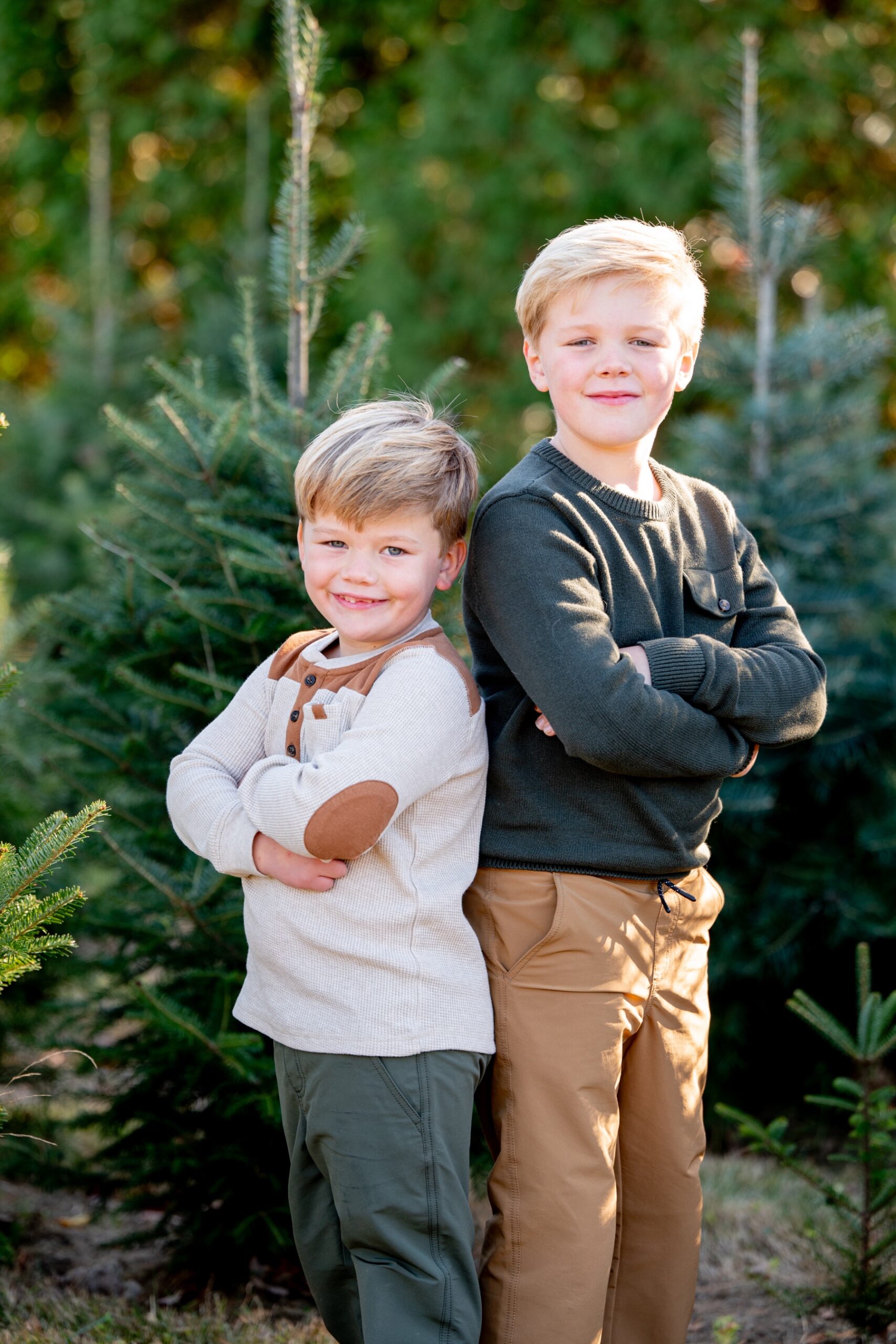 two young boys standing in front of pine trees 