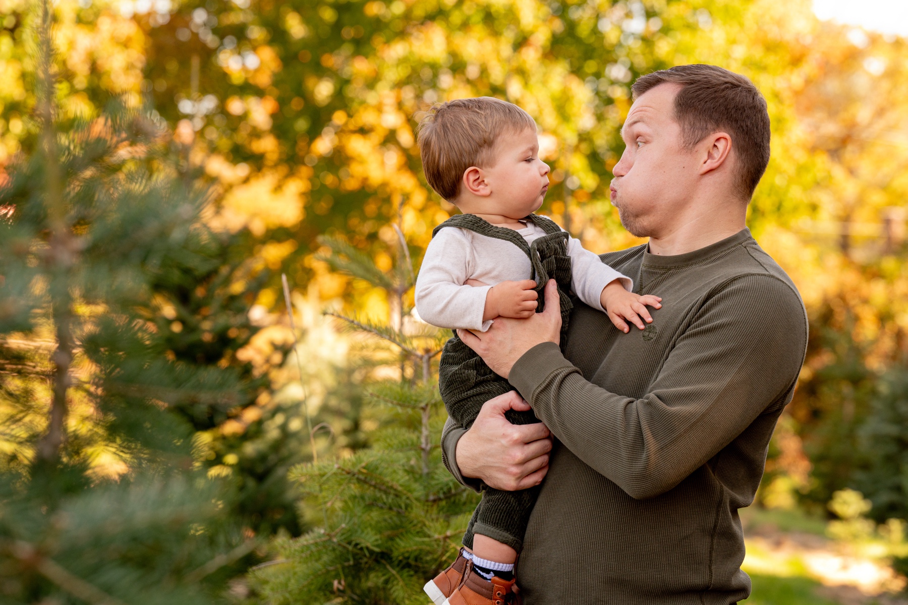 father holding his son and smiling at him with fall foliage behind them 