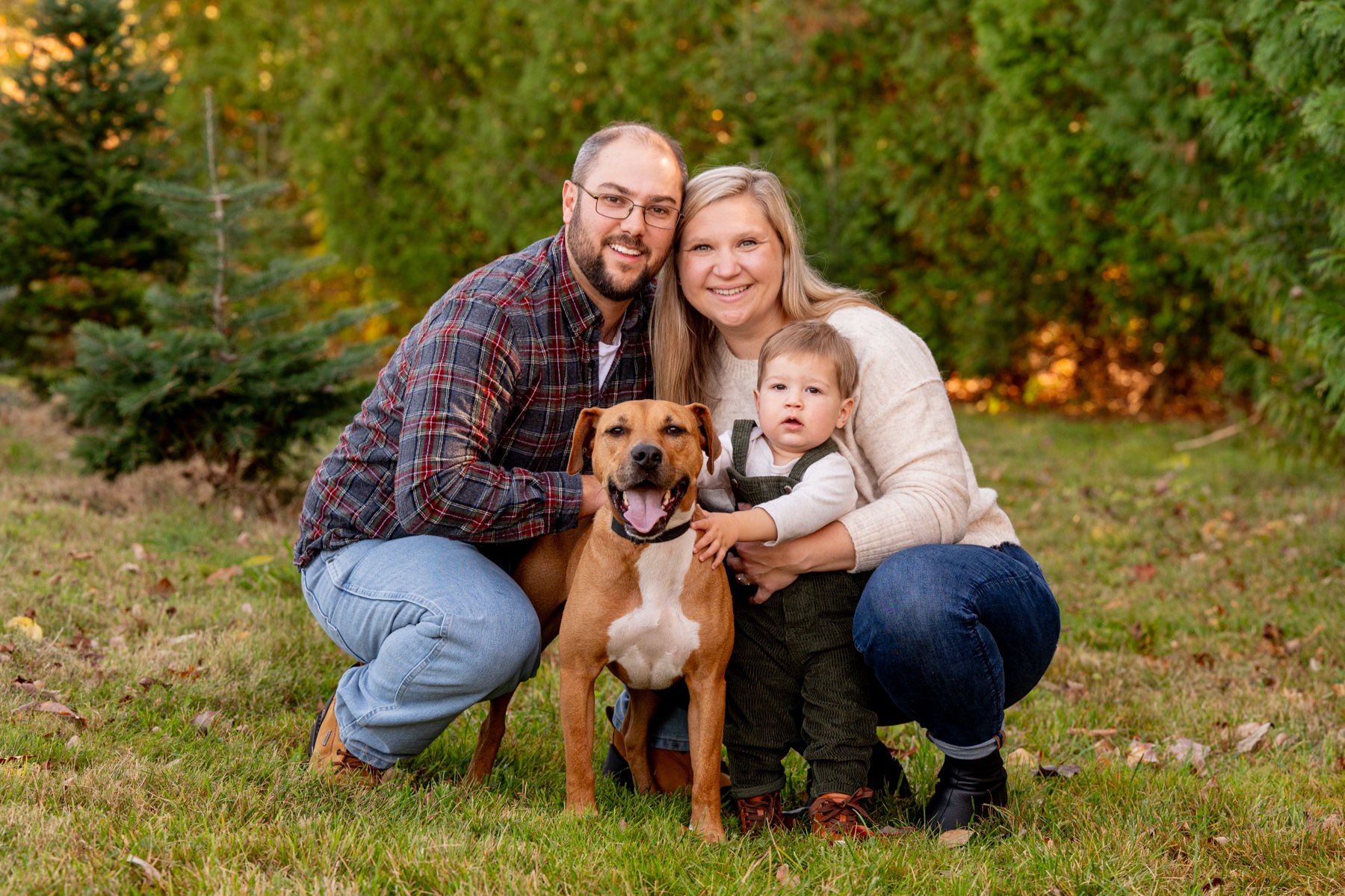 family of three crouching on the ground with their dog 