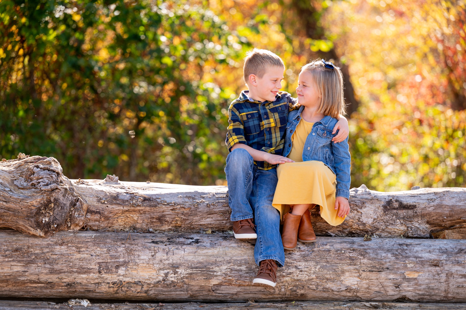 a young boy and girl sitting on a large log