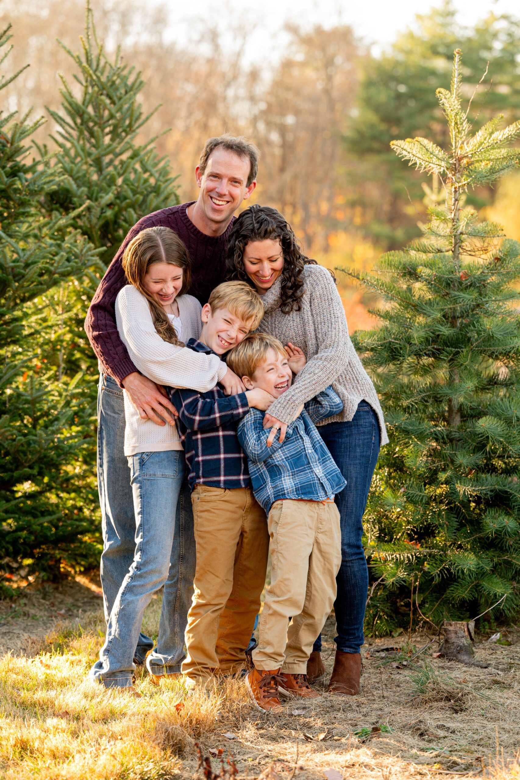 parents hug their three kids while standing at christmas tree farm in stow ma