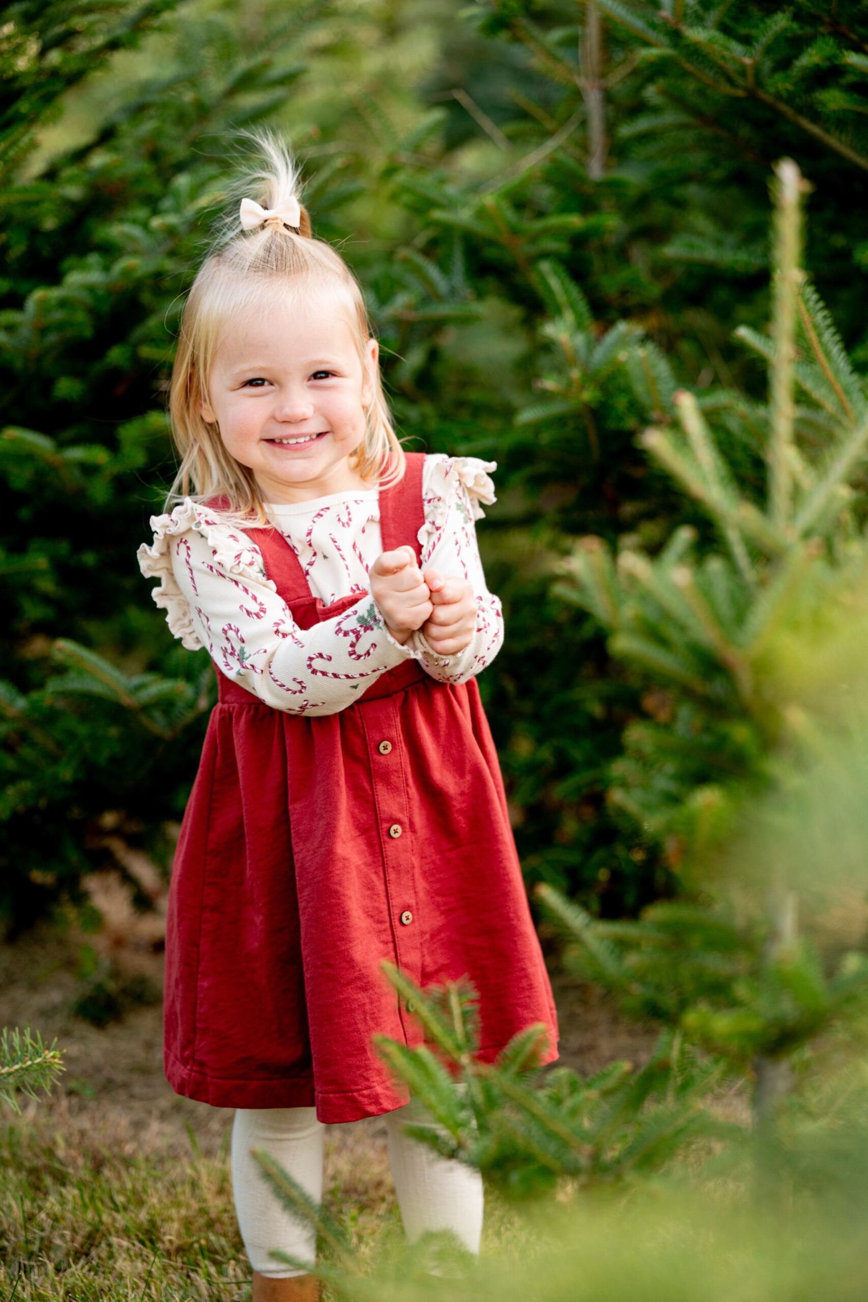 young girl wearing red dress standing next to christmas trees for family photos
