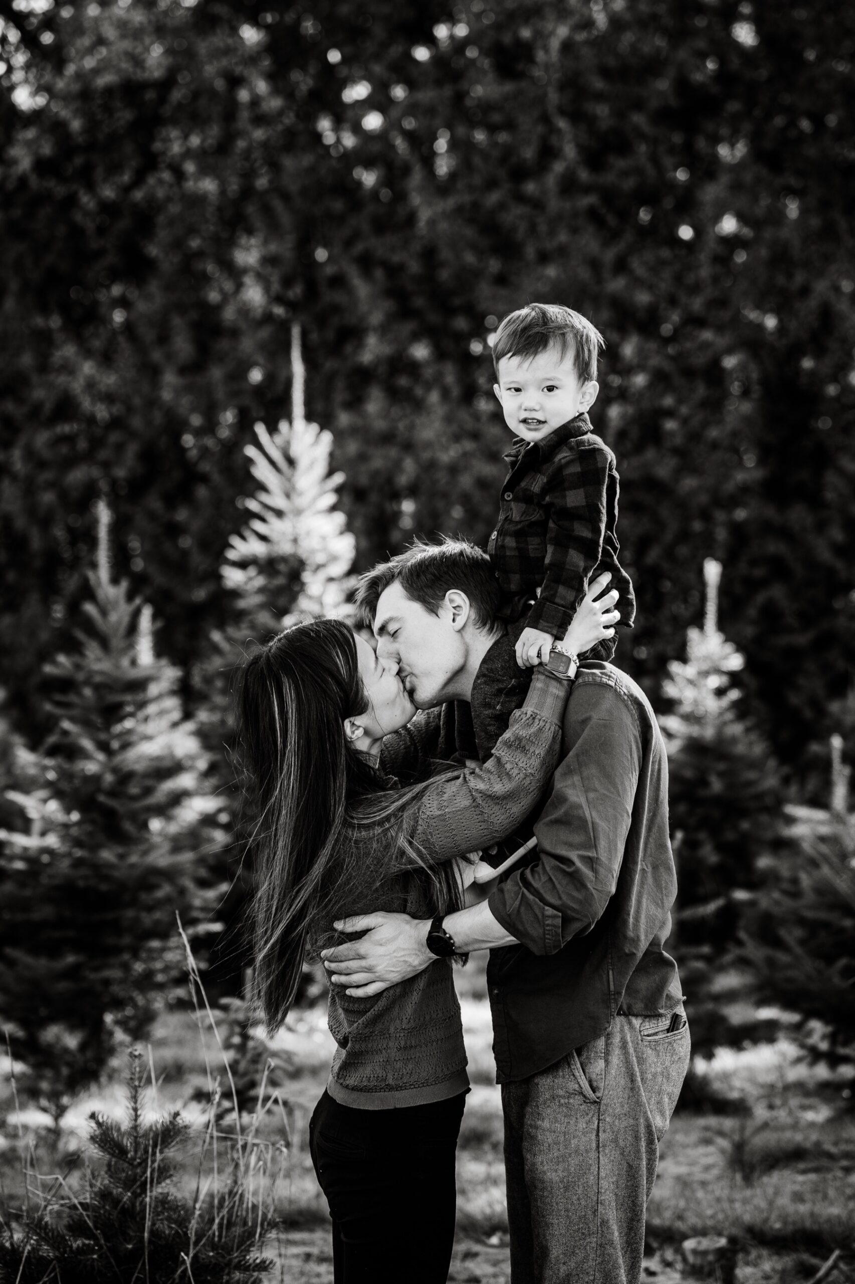 parents standing with young boy surrounded by pine trees