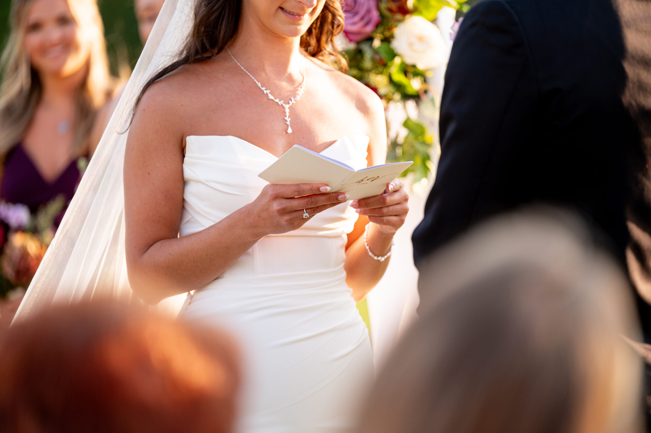 bride holding her wedding vow book during ceremony with sunlight coming in from behind her