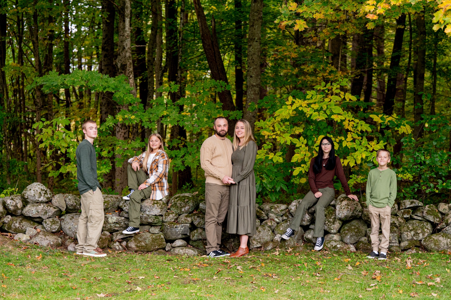 a family of six stands along a new england stone wall