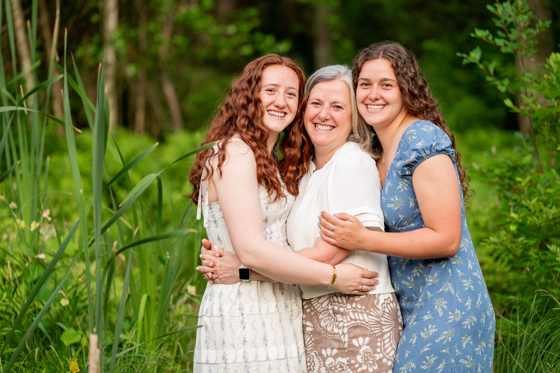 a mom and her two older daughters stand in front of a green yard in sterling ma