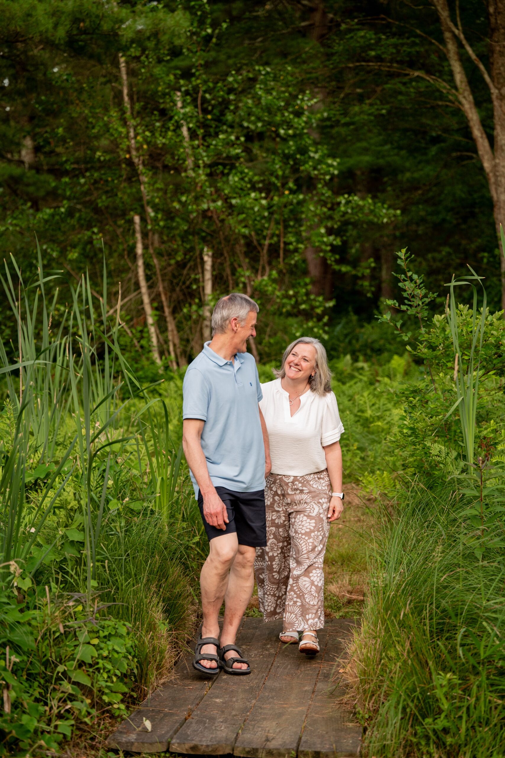 an older couple walks along a woodsy path for a portrait session