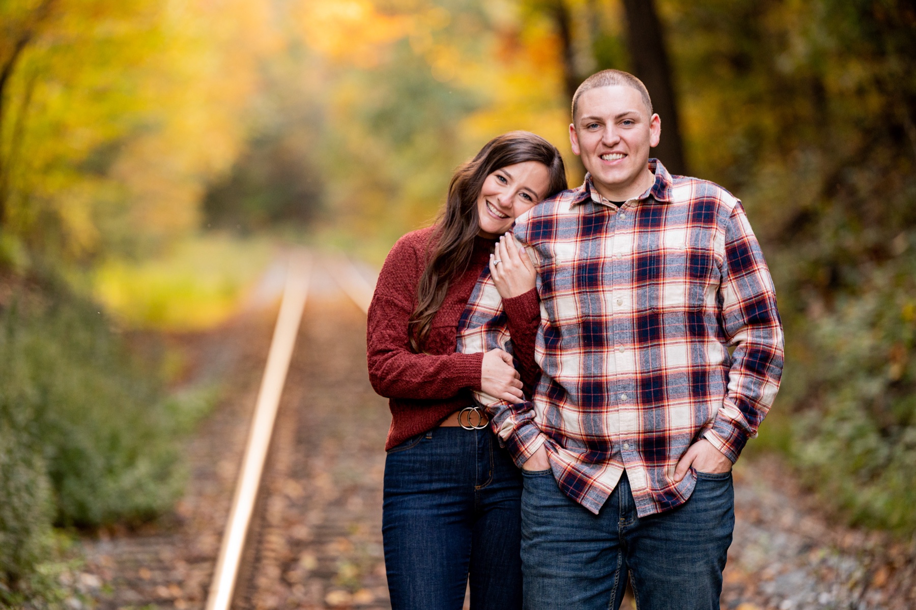 couple poses next to train tracks during an engagement session