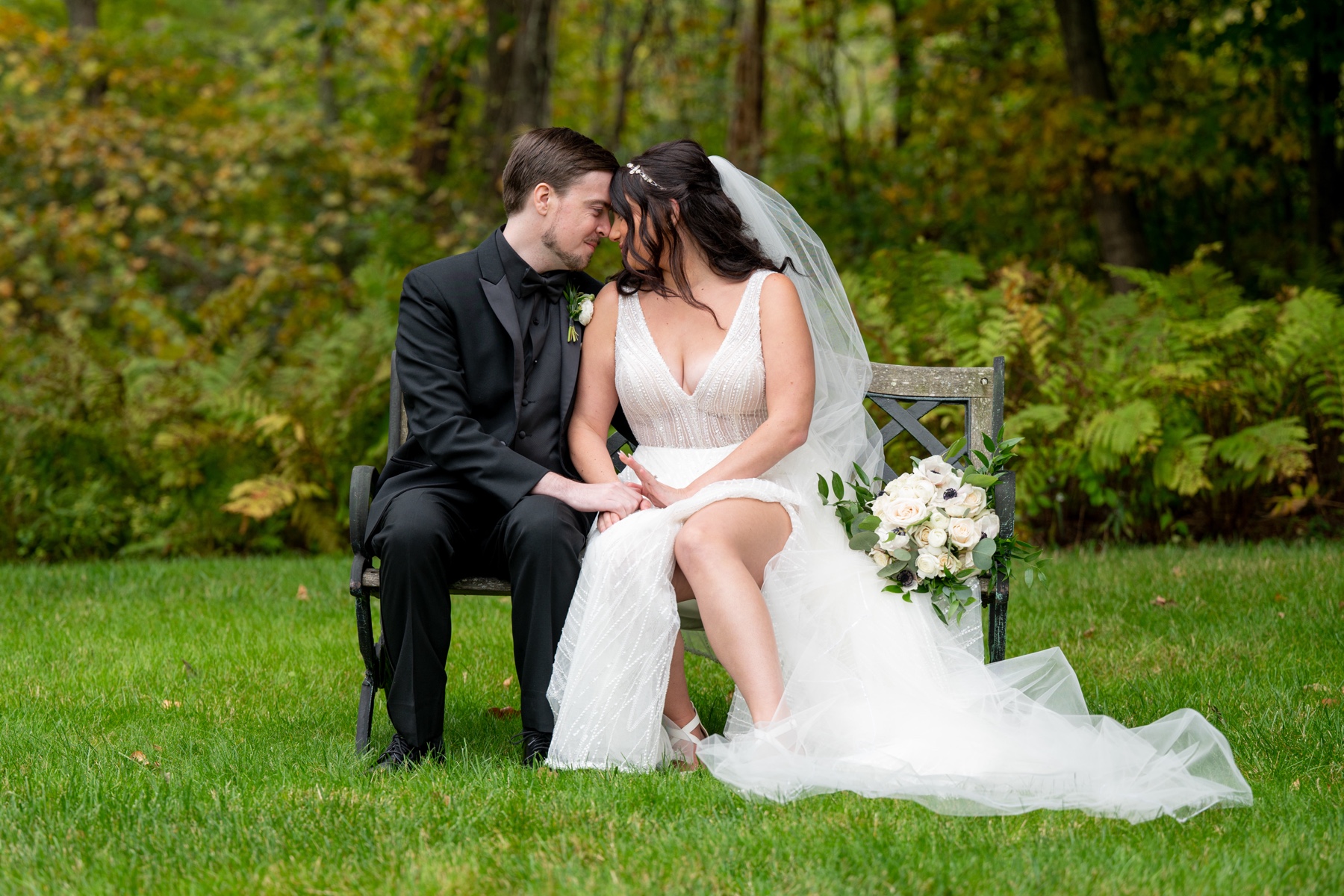 bride and groom sit on bench in grassy backyard
