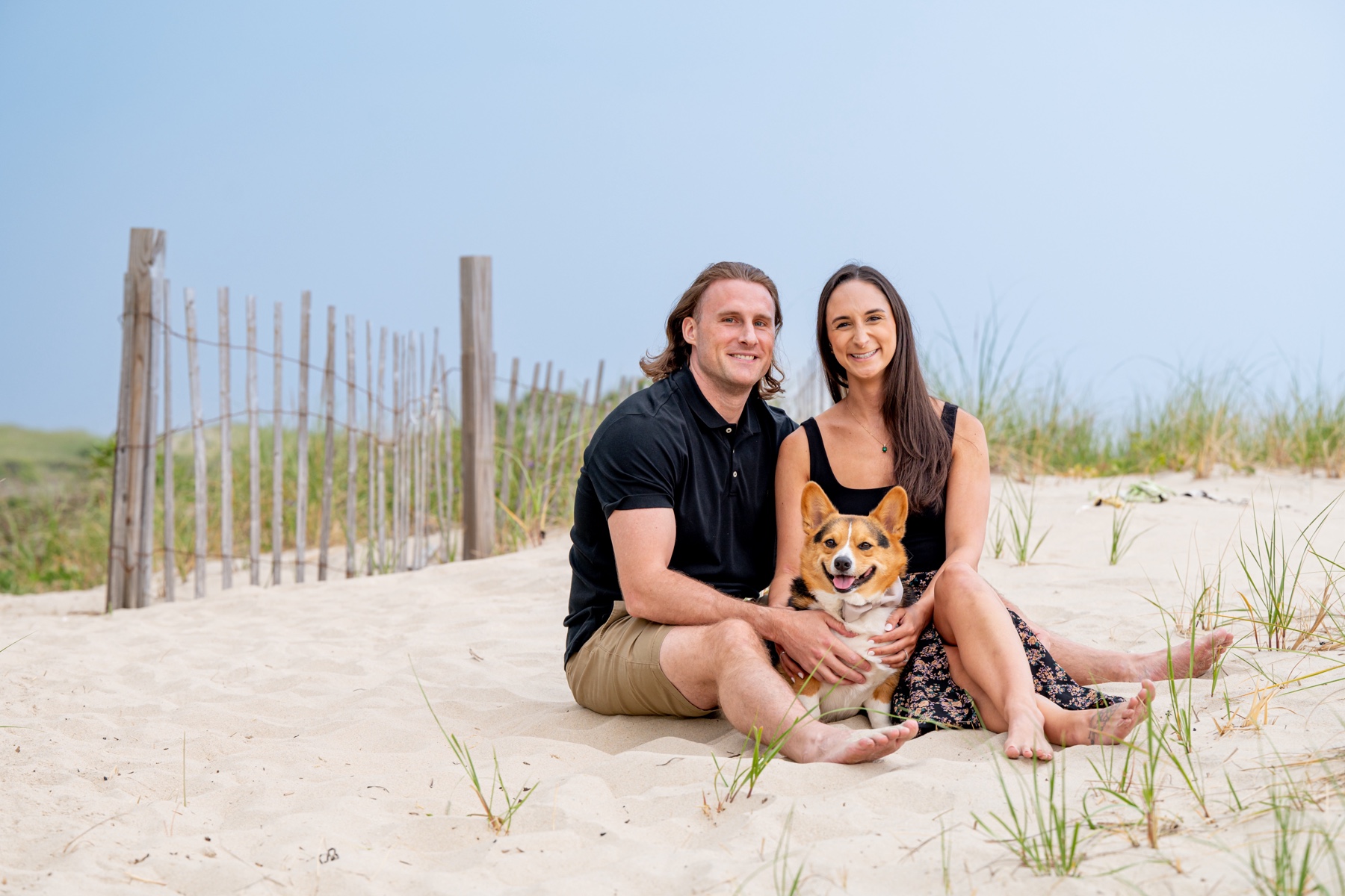 couple sitting on the beach with corgi dog during cape cod engagement session