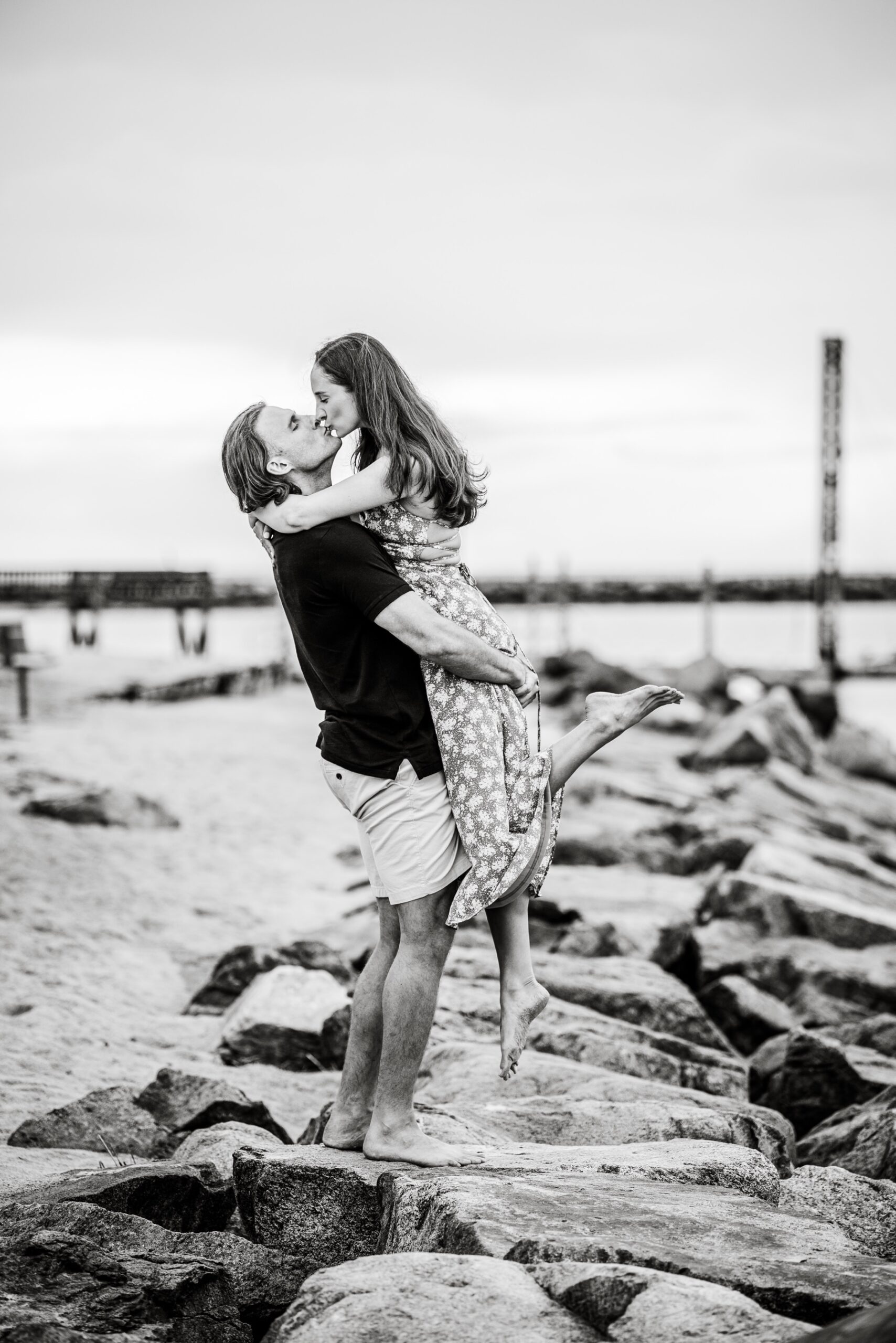 man lifting up his fiance as they kiss on the beach