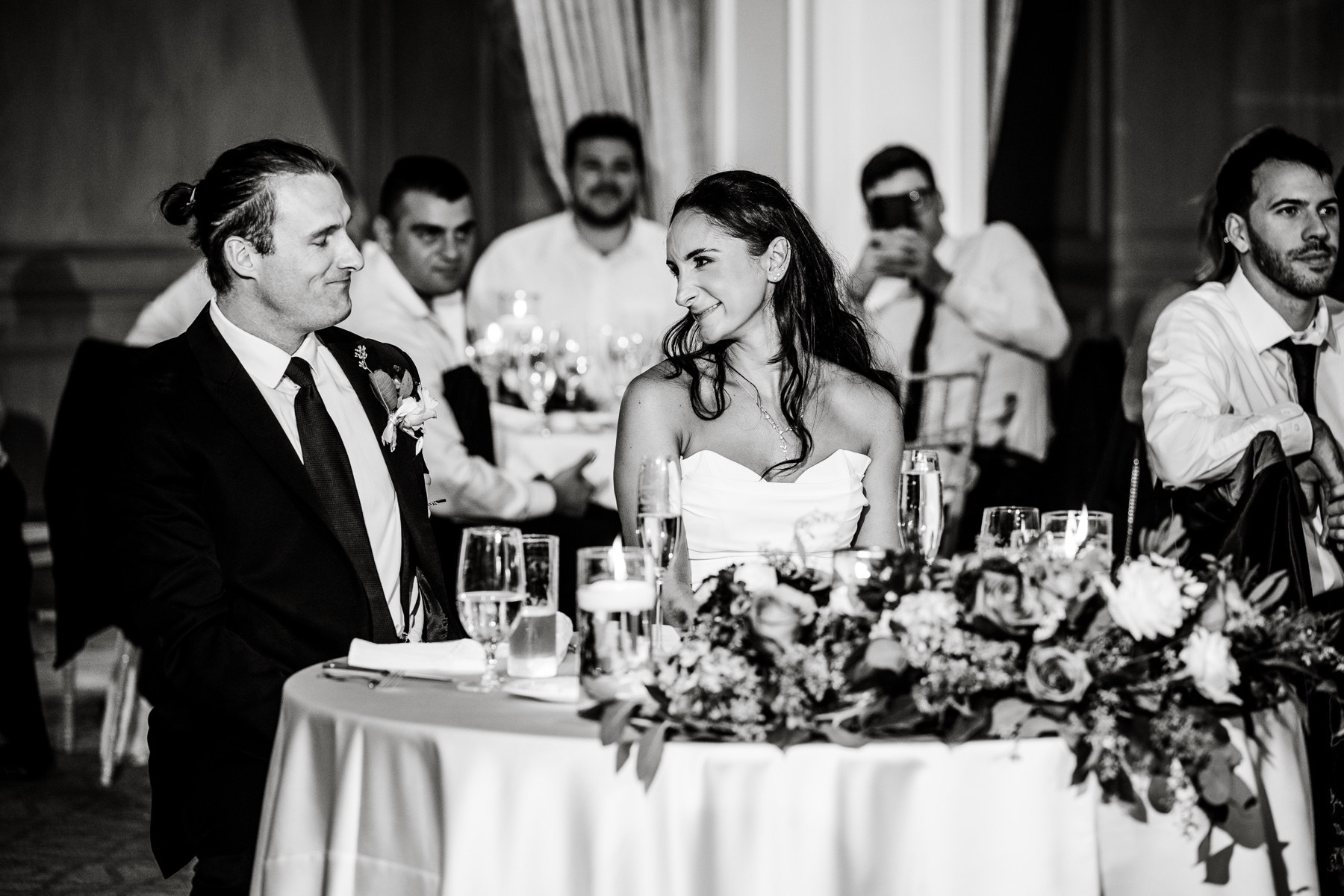 bride & groom smiling at ecah other at their sweetheart table during wedding toasts