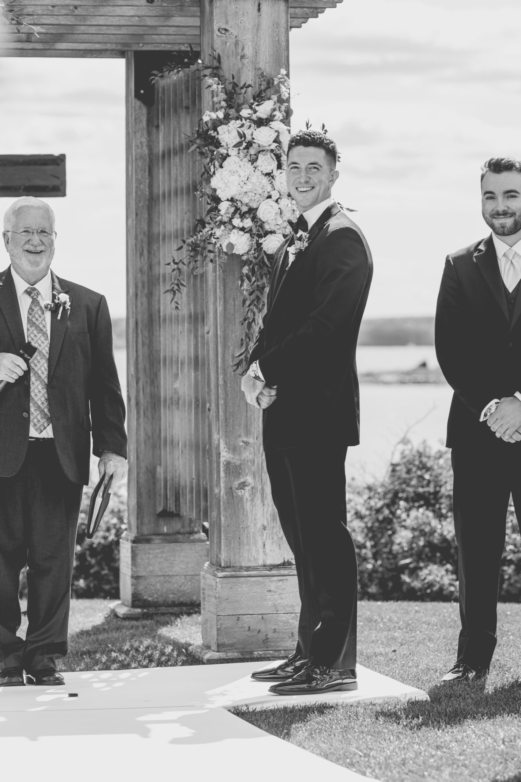 groom standing at end of aisle smiling at his bride