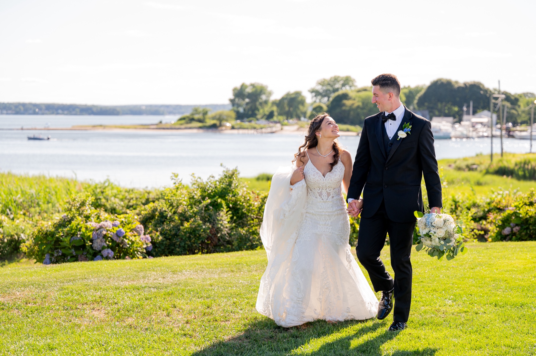bride & groom smiling as they walk along the grass with the ocean view behind them