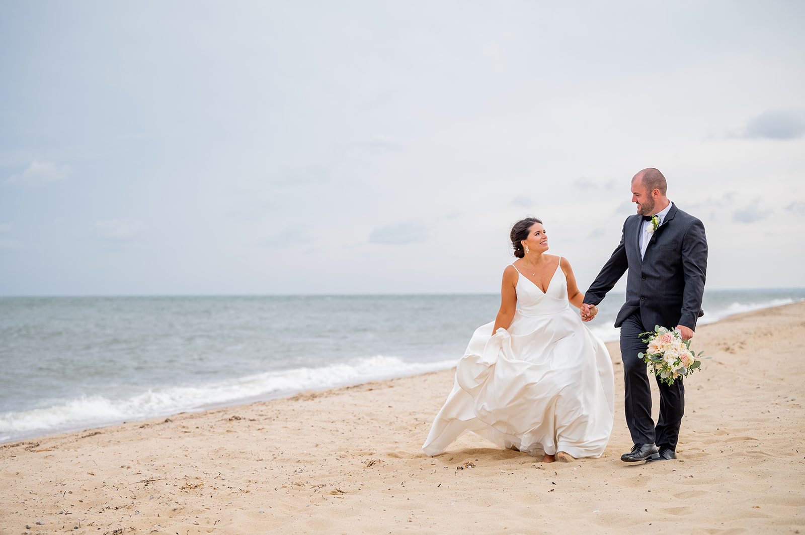 bride & groom walking along a beach holding hands