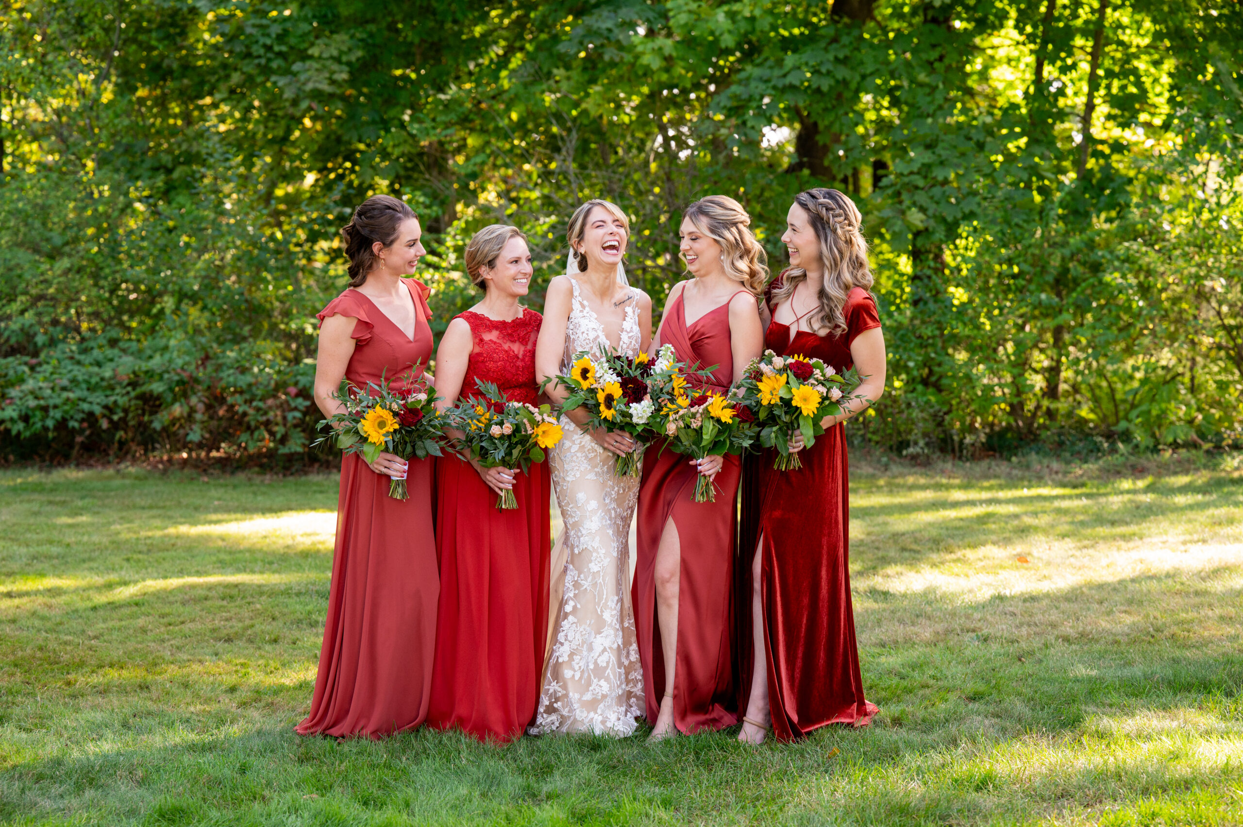 bride with her bridesmaids wearing red dresses outside holding sunflower bouquets 