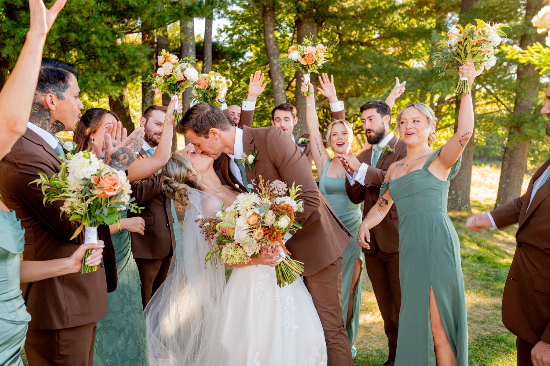 Bride and groom kissing surrounded by cheering bridal party