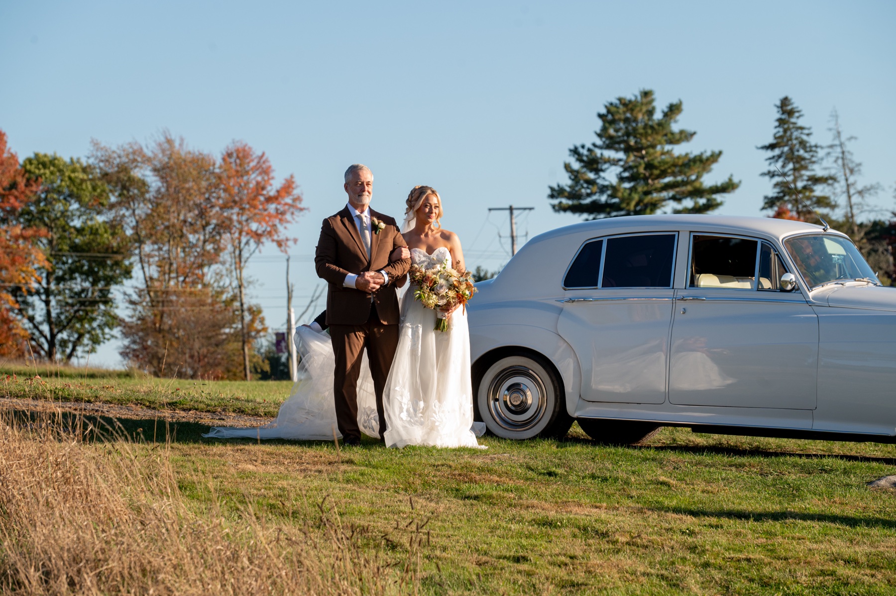 Bride being escorted by her father to the altar - taken on field next to vintage white car