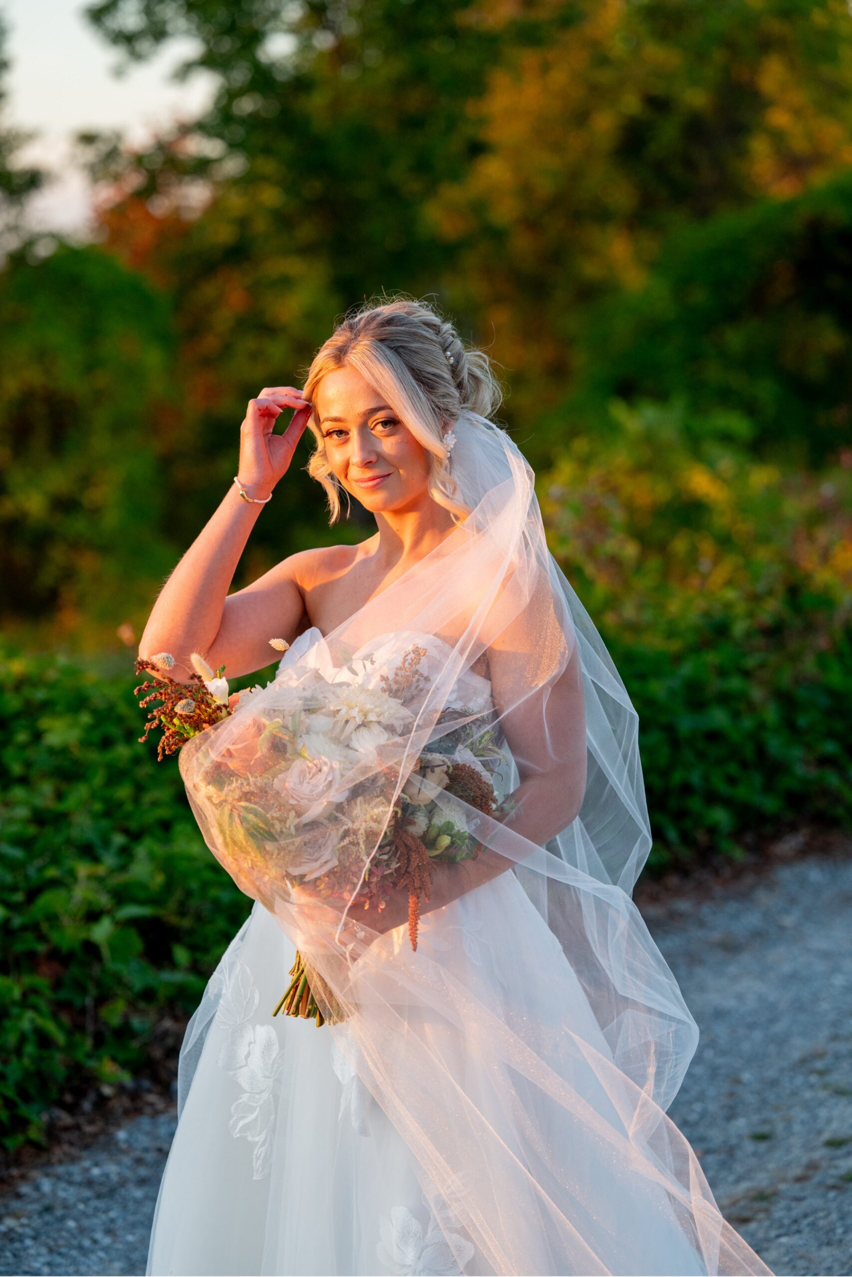 Bride with veil wrapped around her standing on roadway with evening sun on her face