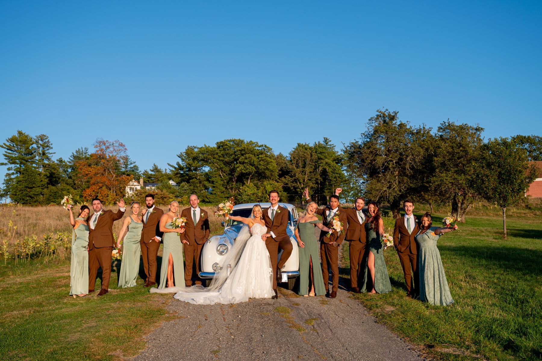 bride and groom with bridal party posing in front of white vintage car