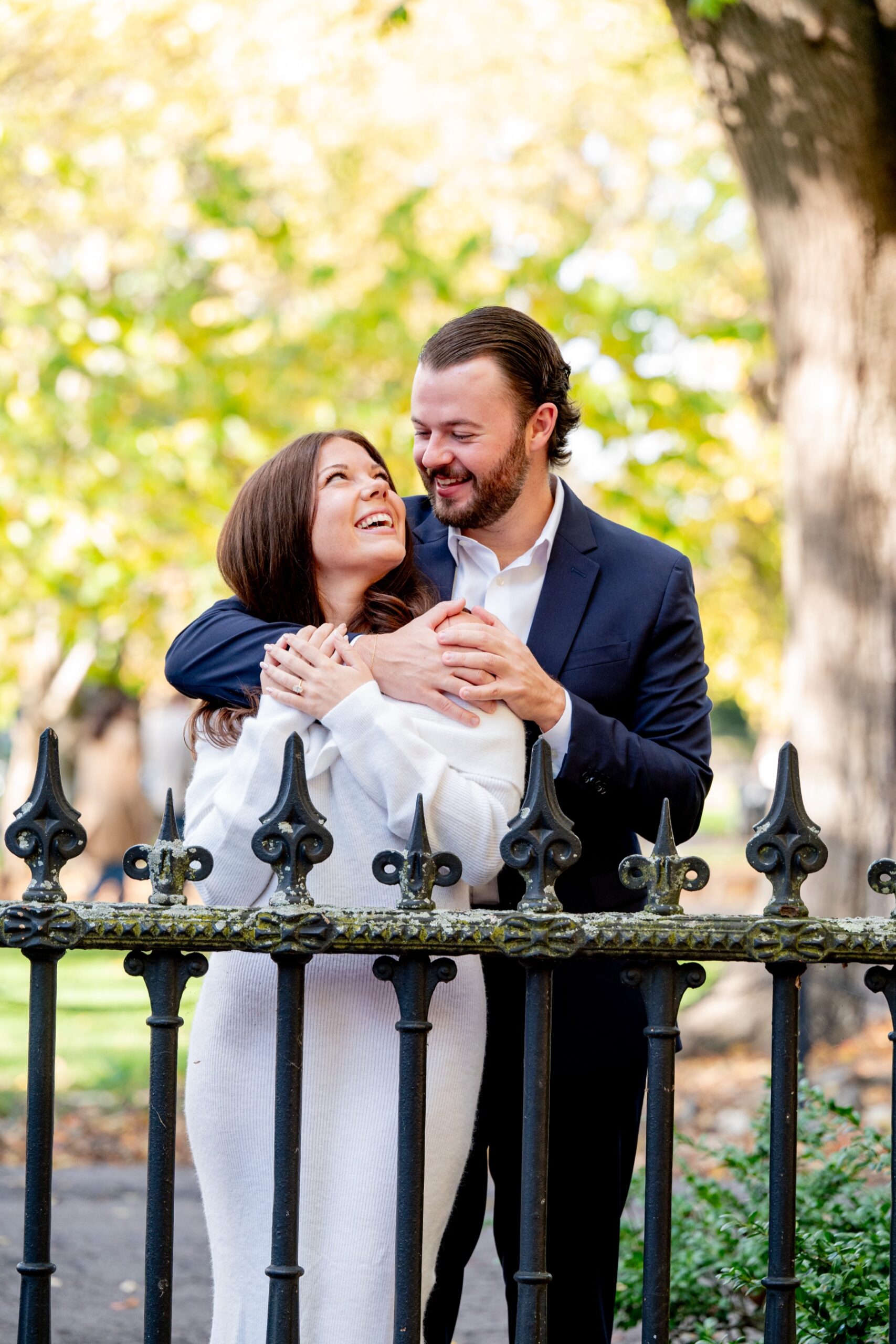 Couple gazing into each others eyes while standing behind a waist height ornate wrought iron fence